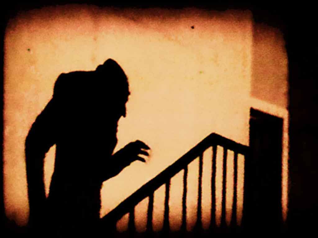 creepy still from old horror film: sinister shadow walks upstairs